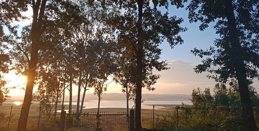 A scenic view of sunset in Umramgso in Assam with a backdrop of mountains and a lake.