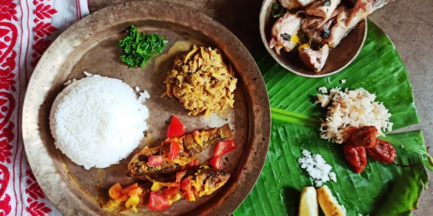 A colourful Assamese lunch platter featuring rice, fish, vegetables, and traditional sides.