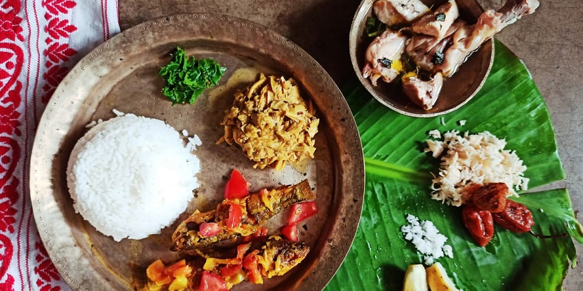 A vibrant Assamese lunch thali featuring rice, non-veg, lentils, and assorted vegetables.