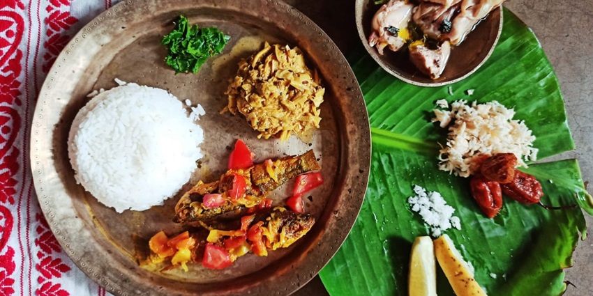 Assamese lunch thali featuring rice, chicken curry, lentils, and colourful vegetables.