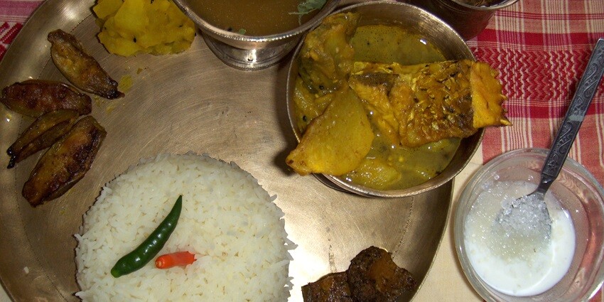 Image of delectable assamese thali served on a golden colour plate with curd and water.