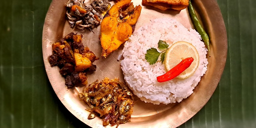 Assamese food thali with an assortment of traditional dishes served on a metal platter.