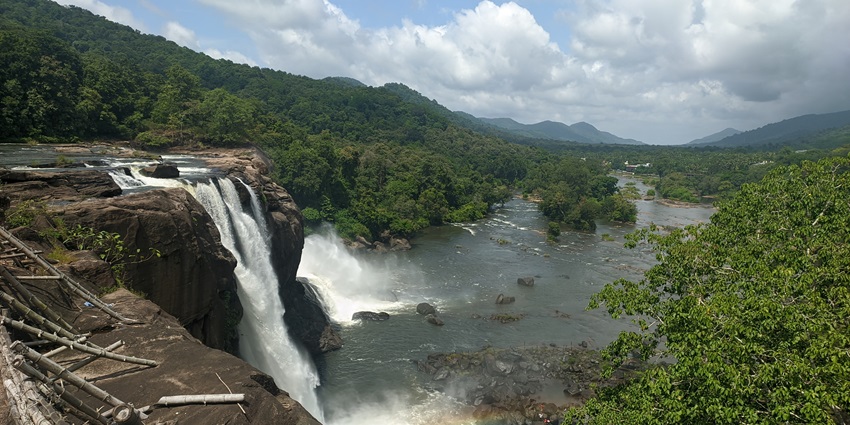 A picture of a huge waterfall in Kerala cascading down a hill, with trees and greenery all around