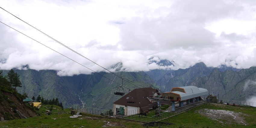 A scenic view of a ski resort in Auli, with tall mountains touching clouds in the background