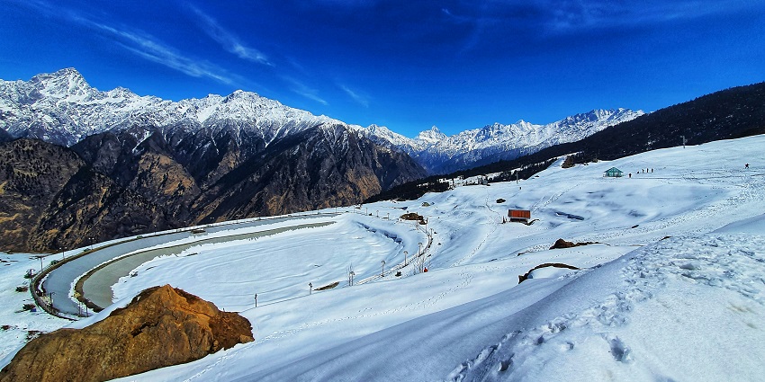 A serene view of Auli featuring snow-clad mountains and frothy white snowy grounds.
