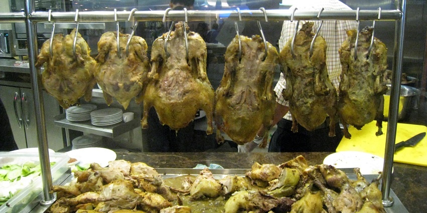 A picture of chickens hanged with a skewer at a restaurant counter