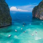 Aerial view of turquoise waters of Thailand dotted with boats and surrounded by peaks.