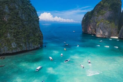 Aerial view of turquoise waters of Thailand dotted with boats and surrounded by peaks.