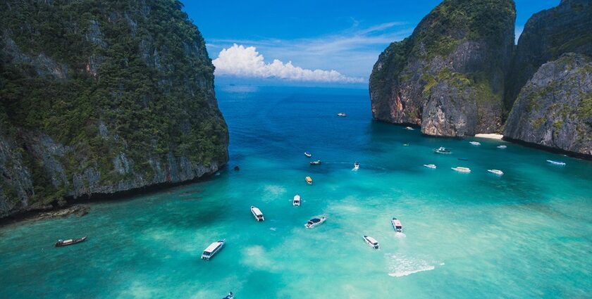 Aerial view of turquoise waters of Thailand dotted with boats and surrounded by peaks.