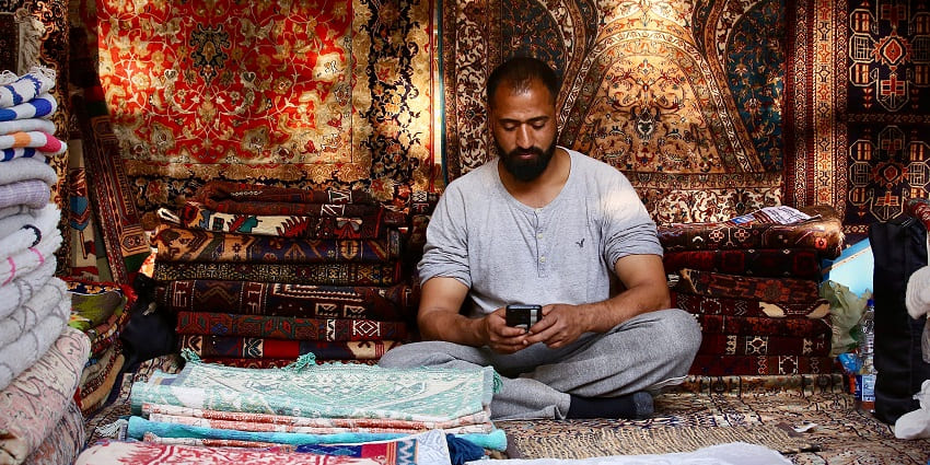 Image of man selling carpets in a market - colourful carpets and designed in a traditional way