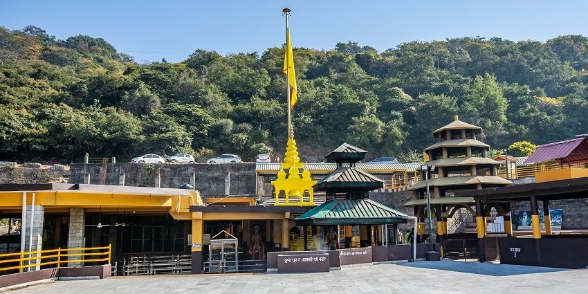 A quaint view of the Bagalamukhi Temple with a backdrop of green-capped mountains.