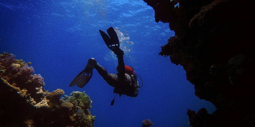 Person submerged underwater, with sunlight filtering through the water's surface.