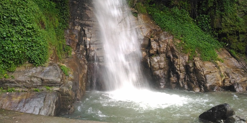 A picture of a beautiful waterfall cascading down a lush green terrain near the Lingdum Monastery 