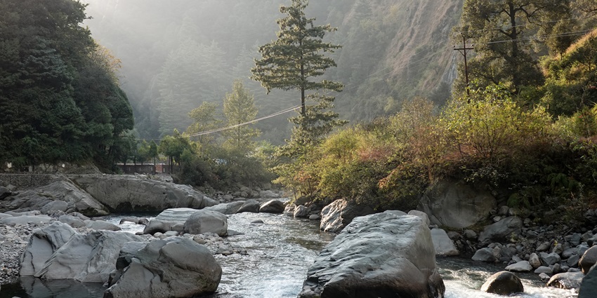 View of a stream of water moving through big boulders and mountains in the backdrop