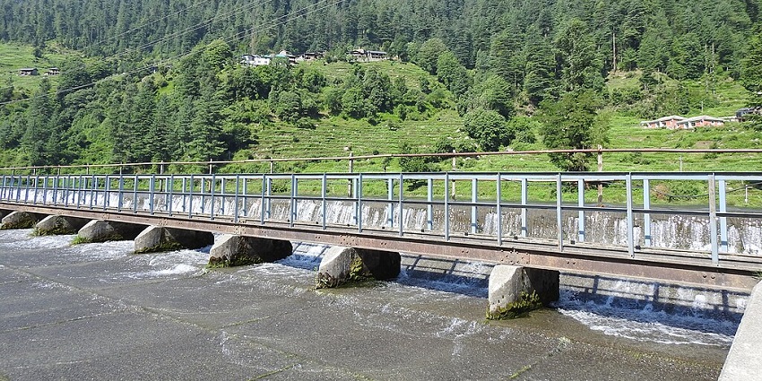 A breathtaking view of Barot Valley featuring lush green vegetation and a dam.