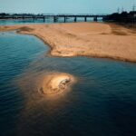 A mesmerising view of a beach with soft sands on the side and a bridge across it.