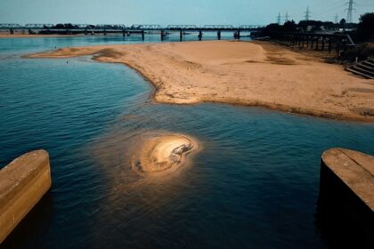 A mesmerising view of a beach with soft sands on the side and a bridge across it.