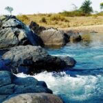 A breathtaking view of a sparkling beach with big and small rocks in it during the day.