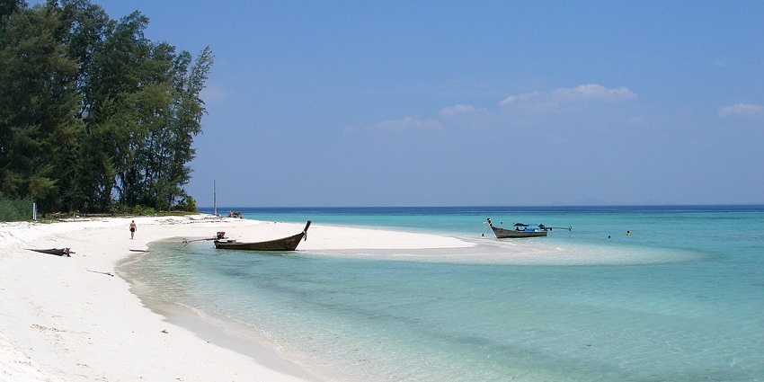 A scenic view of a white sand beach with two boats on the shore and clear skies in Krabi