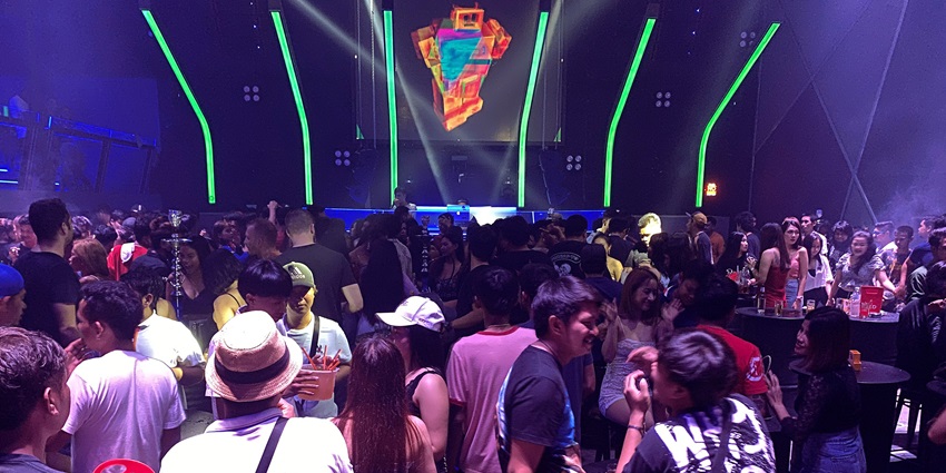 A picture of a nightclub in Bangkok with people seen enjoying under the blue lights