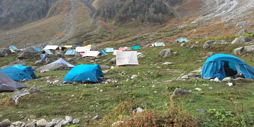 A picture taken at a green mountain with multiple tents placed for campers to rest