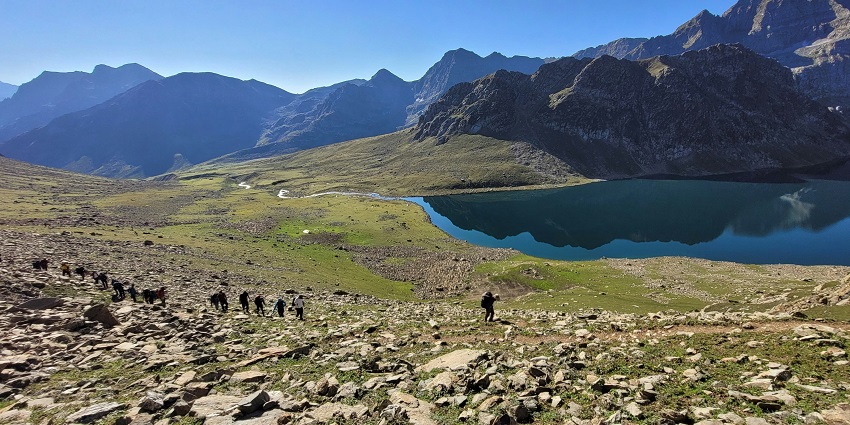 A view of people passing by a beautiful lake with a mountain range in the background.