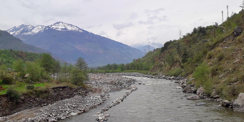 A picture of a river flowing through the majestic hills in Manali with views of the Himalayas in background