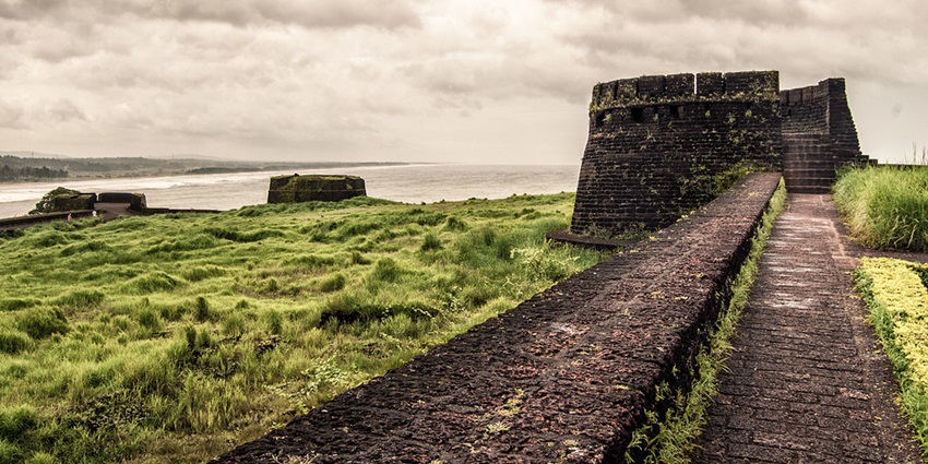 View of the walls of Bekal Fort surrounded by grass on a cloudy day.