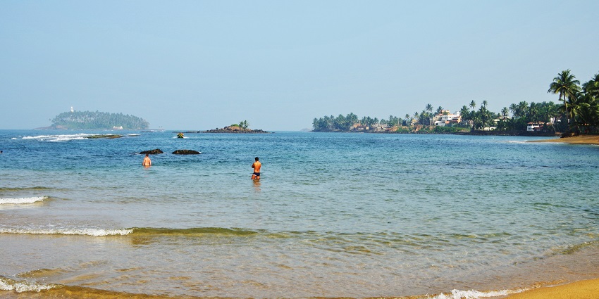 Palm-lined Beruwala beach with golden sand, calm waves, and a peaceful ocean horizon.