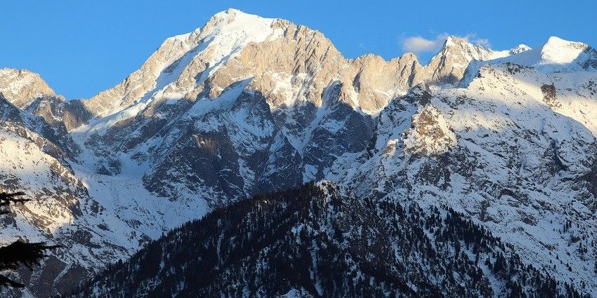 A breathtaking vista of snow-capped mountains and pine trees in Himachal Pradesh.