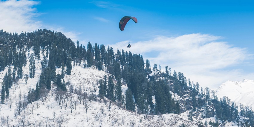 A breathtaking view of a person paragliding over snow-covered mountains during the day.