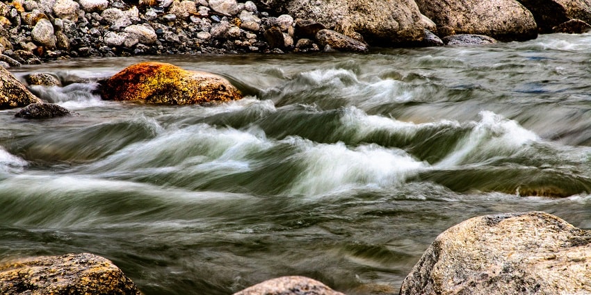 A stunning view of a stream of water with small rocks with mountains in the background.