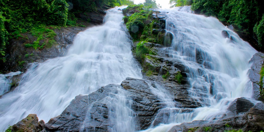 A breathtaking view of a waterfall flowing through rocks surrounded by lush greenery.