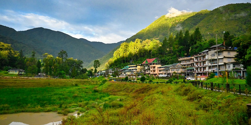A view of colourful houses in Sikkim encircled by lush green meadows during the day.