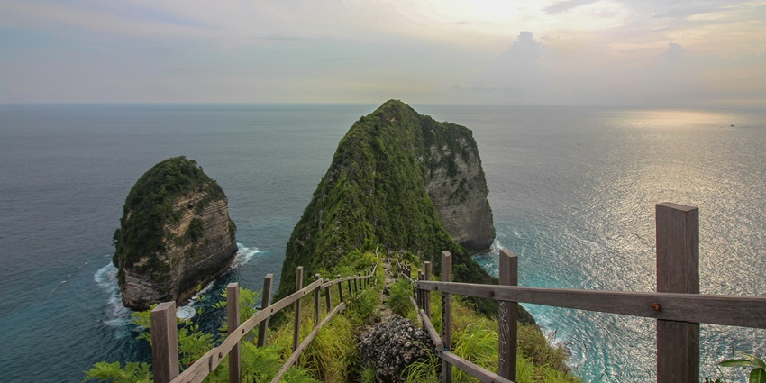A stunning view of a turquoise water body with a lush green cliff and a wooden path.