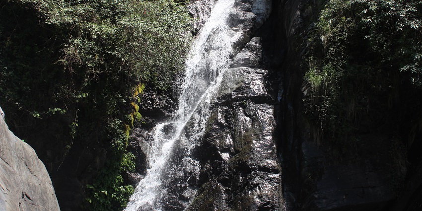 An enchanting view of Bhagsu Waterfall surrounded by lush greenery during the daytime.