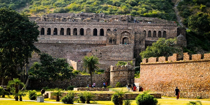 A view of the palatial Bhangarh Fort surrounded by lush greenery and rustic hills.