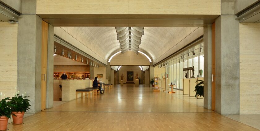 A picture of a museum's interiors showing a long hallway with people admiring art