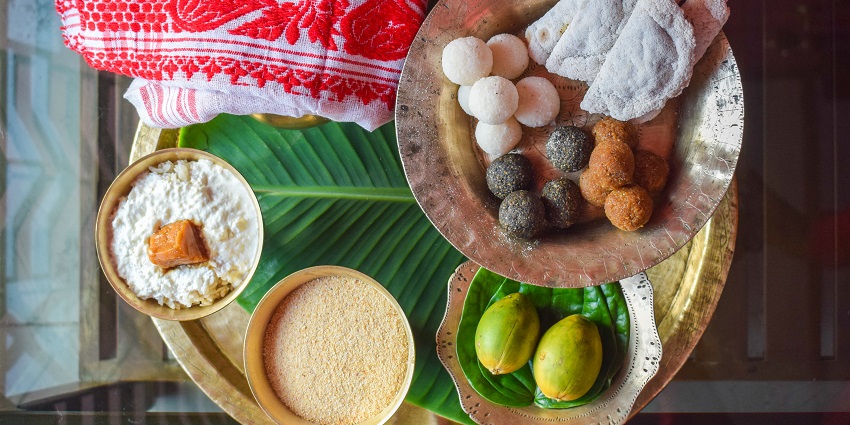 Festive Bihu table with assorted delicacies, including rice cakes and sweets.