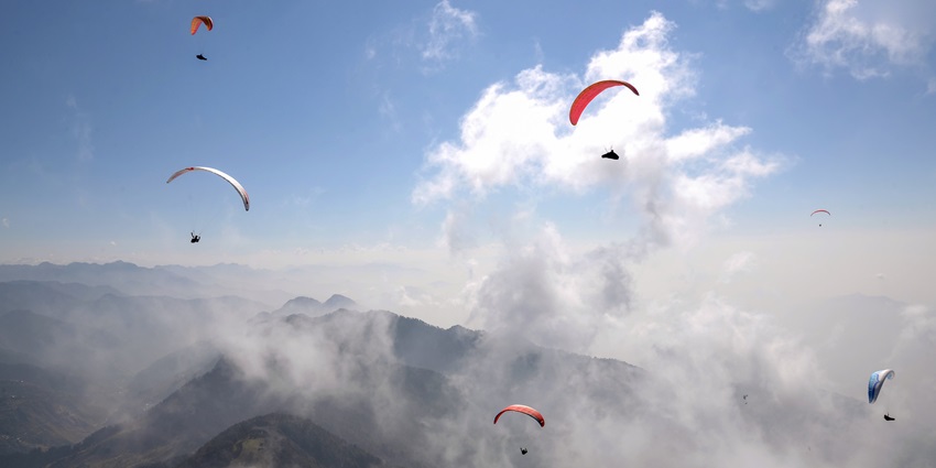 An aerial view of various paragliders in the cloudy sky of Bir, Himachal Pradesh