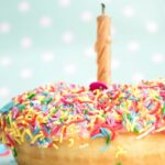 A tempting view of a mouthwatering donut with colourful sprinkles on top with a candle.