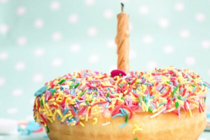 A tempting view of a mouthwatering donut with colourful sprinkles on top with a candle.