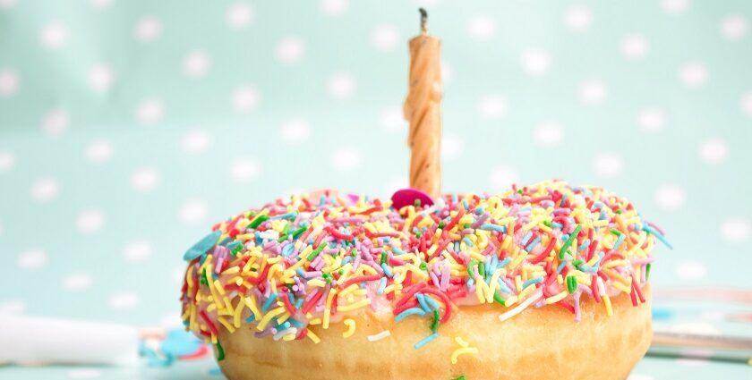 A tempting view of a mouthwatering donut with colourful sprinkles on top with a candle.