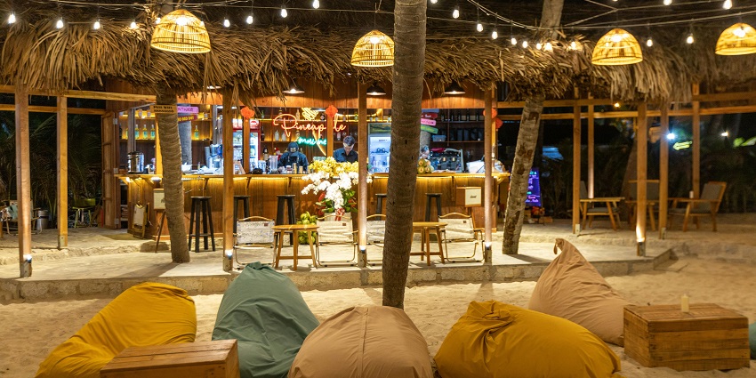Restaurant on a beach with tables and chairs set up for dining near the ocean.