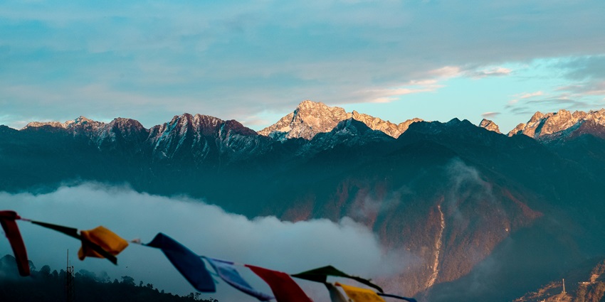 Panoramic mountain view with towering peaks, lush valleys, and a clear blue sky.