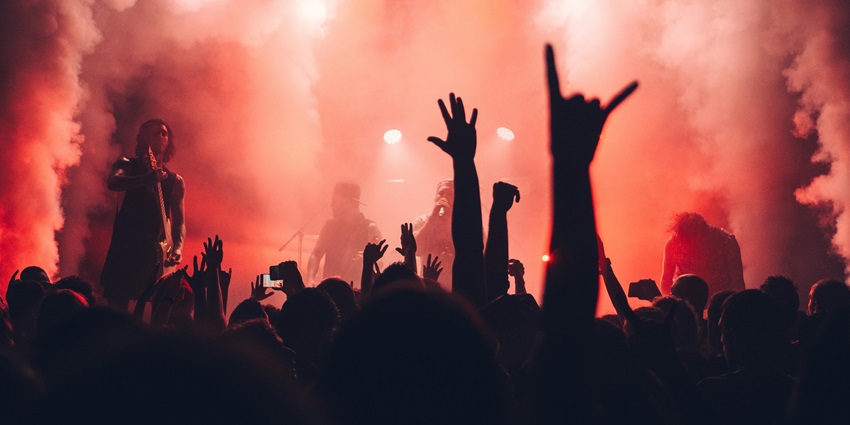 Crowd silhouettes raising hands at a concert, illuminated by colourful stage lights.