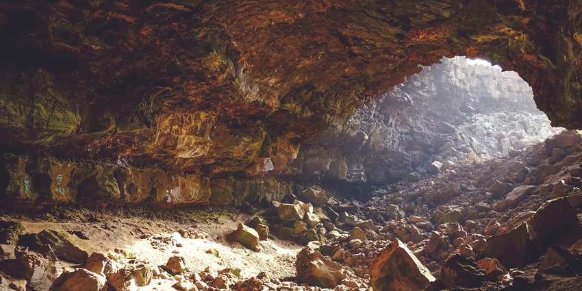 A beautiful image of a cave with rocks lying around and sunlight falling inside.