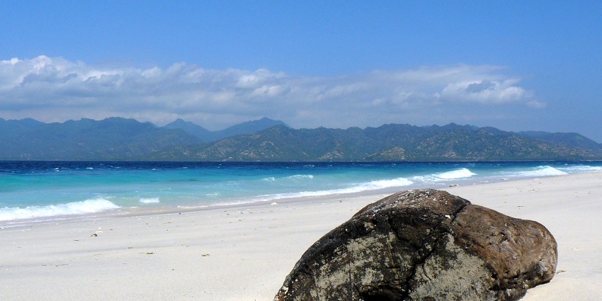A beautiful beach with a big rock and a mountain range in the background