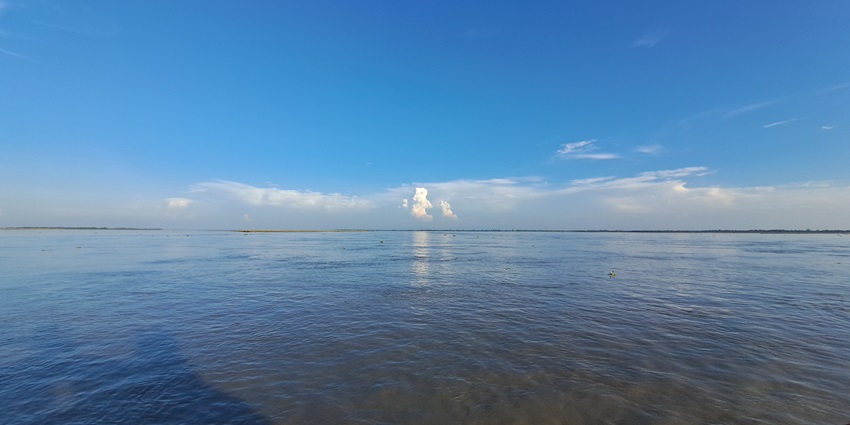 Expansive view of the Brahmaputra River with calm waters and distant green hills.