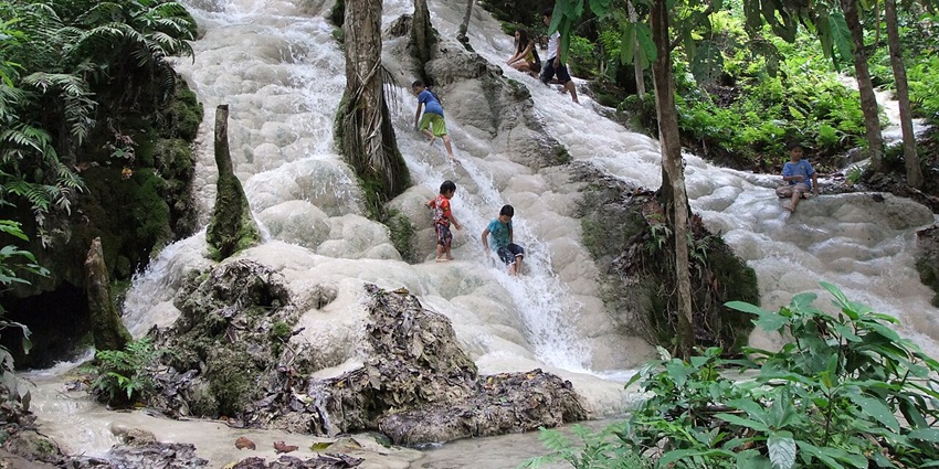 A picture of a mesmerising waterfall cascading down a lush green hill, with people enjoying